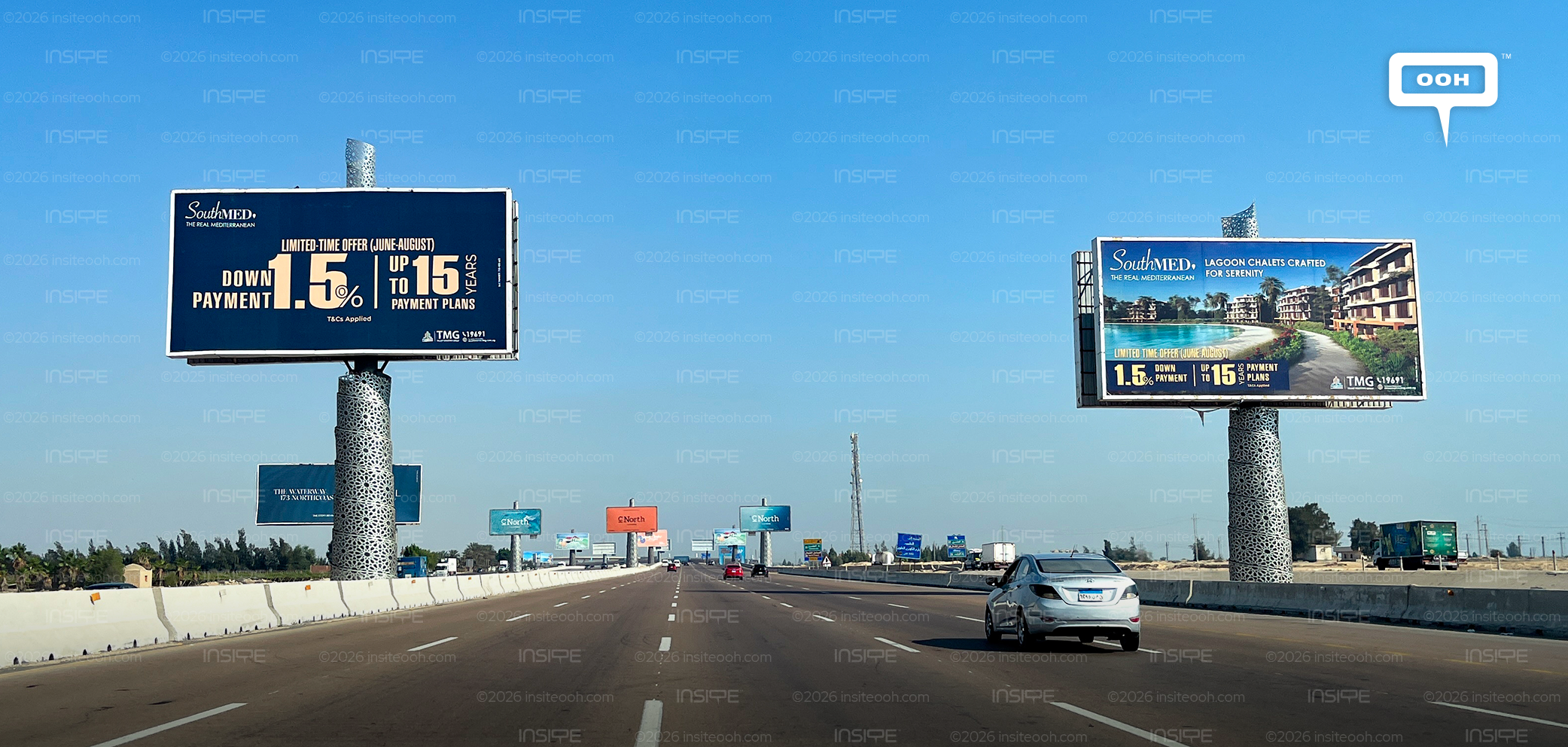 SouthMED billboards on the desert road, one showing a 1.5% down payment and 15-year payment plan, the other the project lagoon and architecture